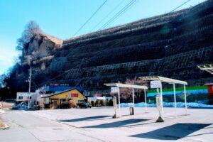 万座・鹿沢口駅 東南側にある路線バスロータリー。背後がきれいに造成されているのは、沿線の周辺と同じくかつて激しい岩壁だったのが崩れ落ちて人が数人亡くなったからとのこと。それからがけ崩れ防止のために、(10~20年ほど?の)長い年月をかけ、現在のような造成にしたらしい。地元の人から教えてもらった。そして、この時は気づかなかったが、この駐車場内にそのがけ崩れの説明と工事竣工記念碑の石碑があったらしい。<笹平地区の大規模崖崩れ:昭和41年7月30日発生>